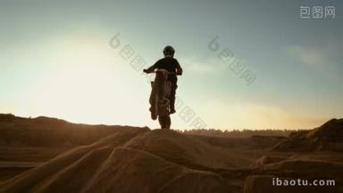 专业摩托车越野摩托车骑手在沙丘上行驶和进一步下跌的越野的轨道。它是日落和轨道上布满烟雾 / 雾.